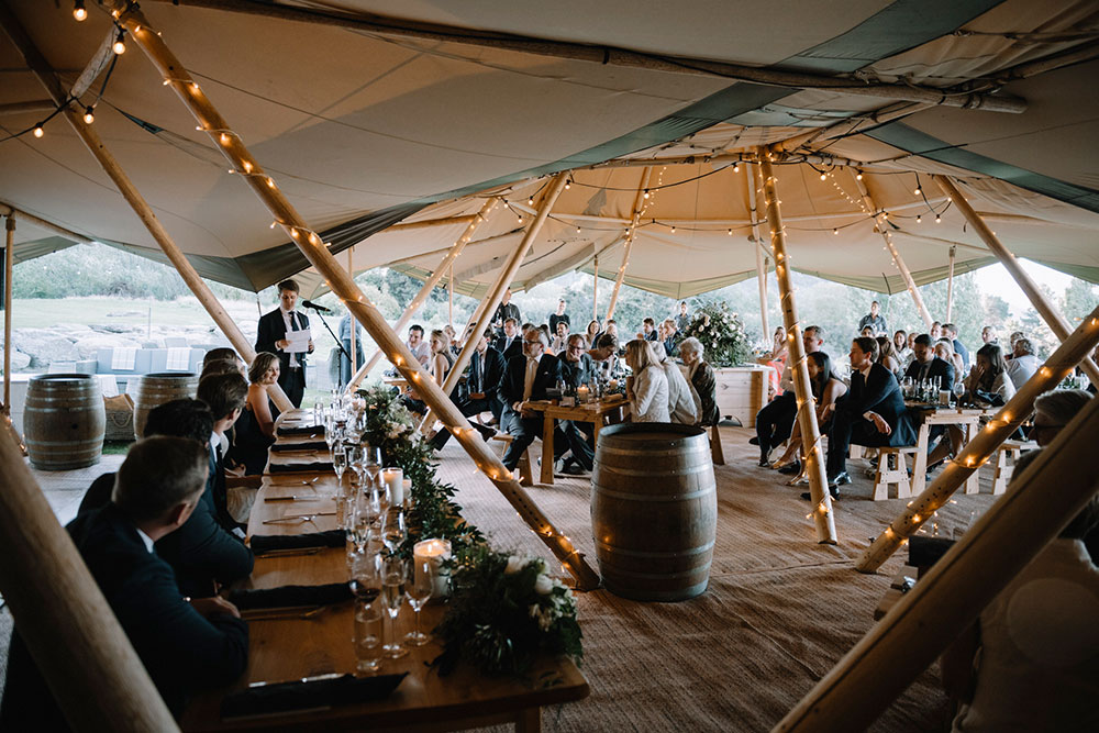 Tipi wedding by Gather and Gold - wedding reception and speeches in large furnished tipi with guests seated at table