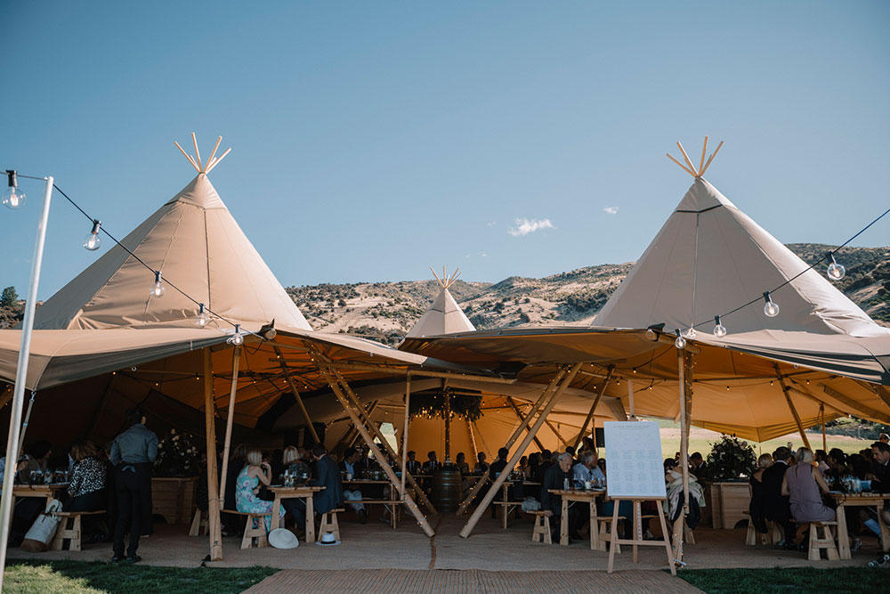 Tipi wedding by Gather and Gold - wedding reception with guests seated in large furnished tipi with sides open