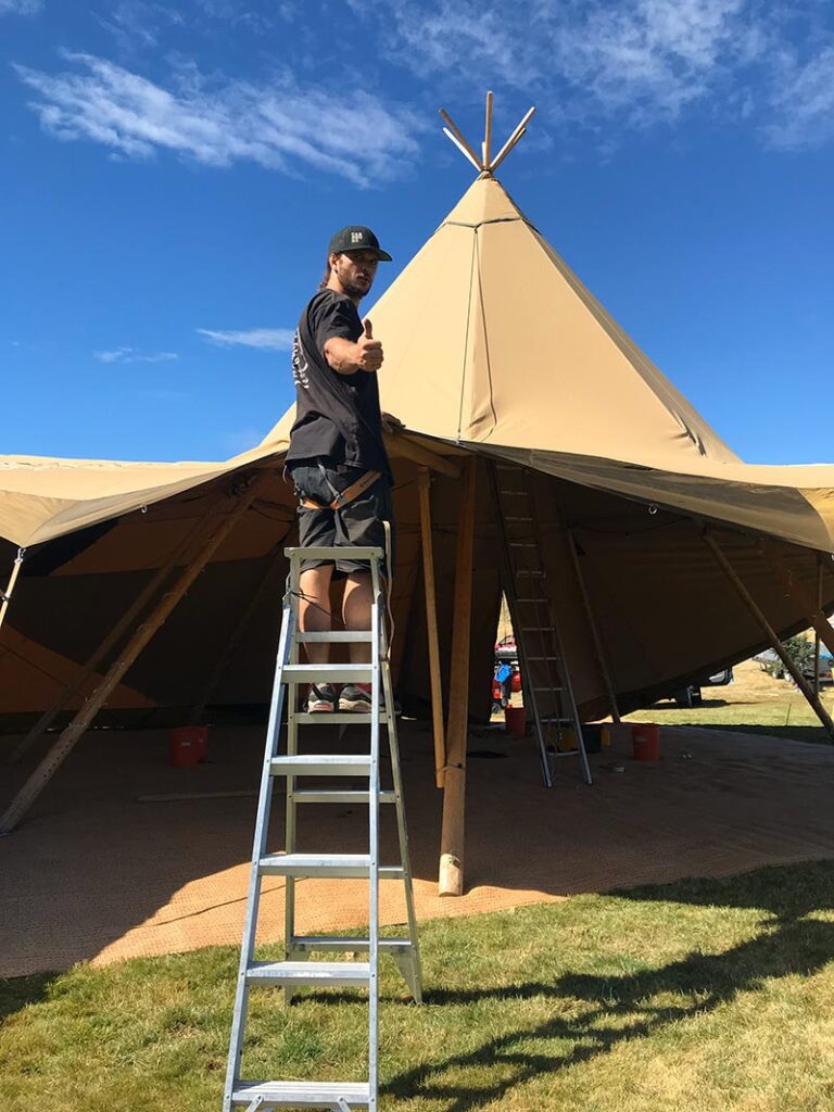 Gather and Gold teepee weddnig venue - man up a ladder setting up a tipi