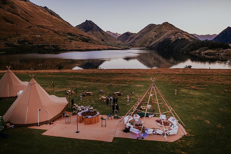 Tipi wedding next to Moke Lake in Queenstown, New Zealand. 2 large covered nordic tipis, and one tipi frame with outdoor sofas and furniture set up. By Gather and GOld