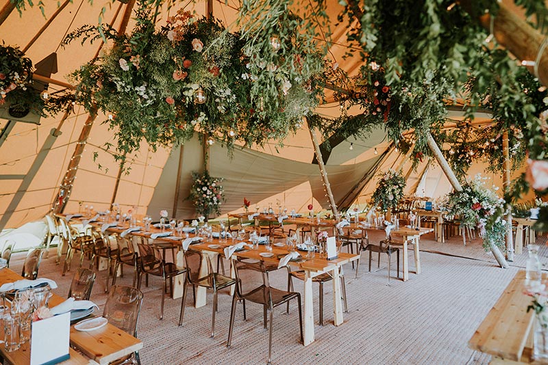 Stunning wedding reception set up with long tables, and hanging flowers inside large nordic tipi from Gather and Gold