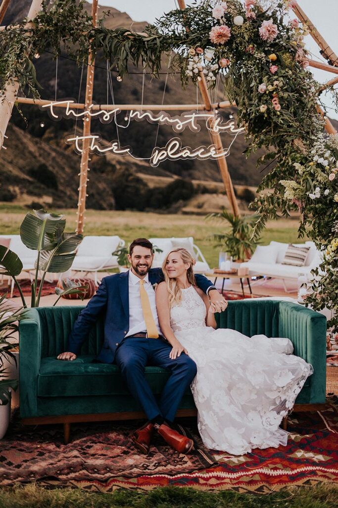 Bride and Groom on sofa inside tipi frame with "this must be the place" sign above them. Tipi hire for weddings by Gather and Gold