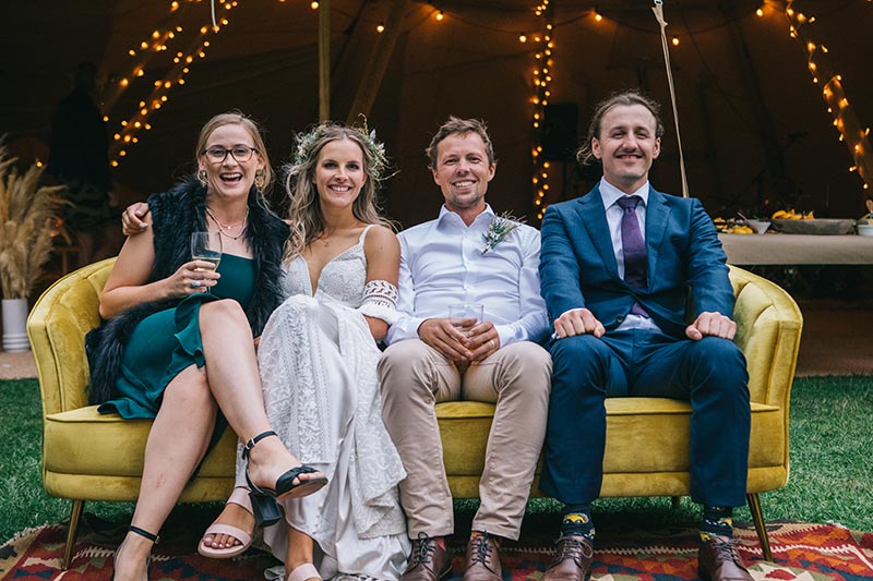 Wanaka tipi wedding by Gather and Gold - bridal party sit on sofa outside large tipi