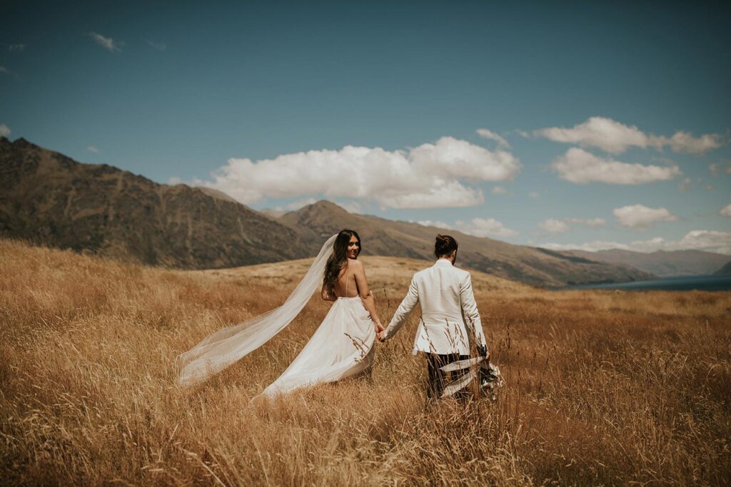 Gather and Gold Teepee hire wedding bride and groom holding hands in a field in Queenstown