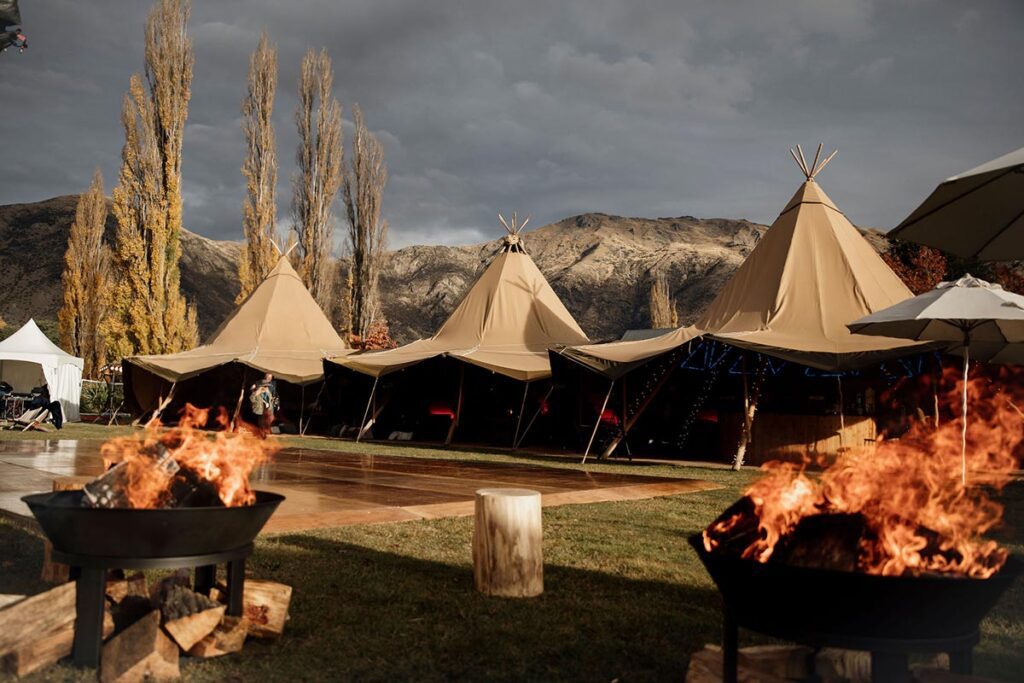 Three gather and gold tipis with two fire pits and a dance floor at a corporate event