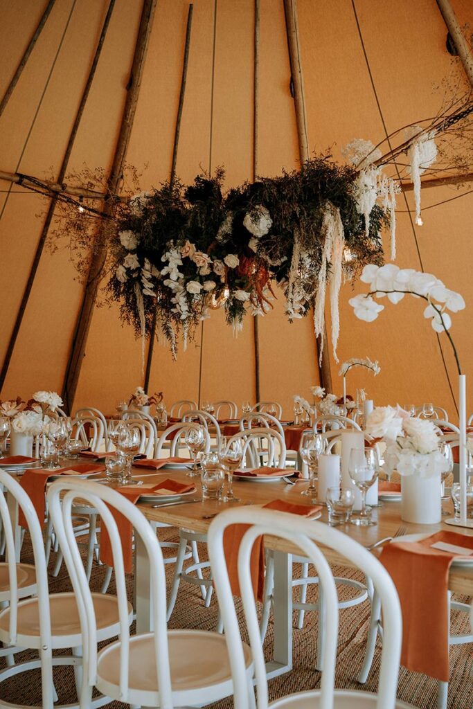 Tipi wedding reception with tables and chairs and hanging floral arrangement