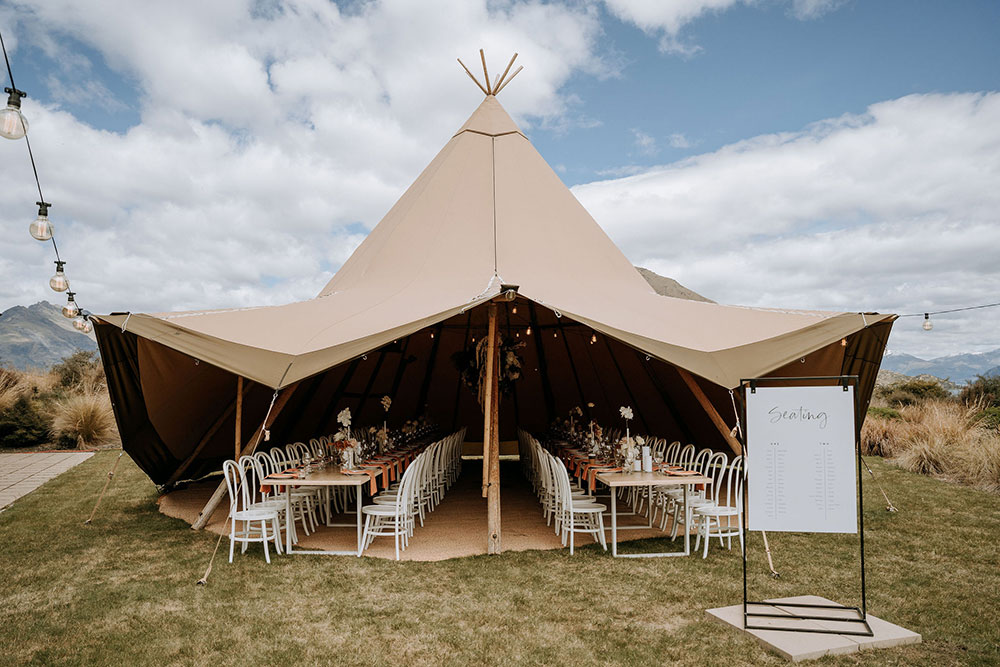 Large bell teepee with open sides as wedding reception venue. Long tables set up with chairs and table settings. Teepee hire from Gather and Gold