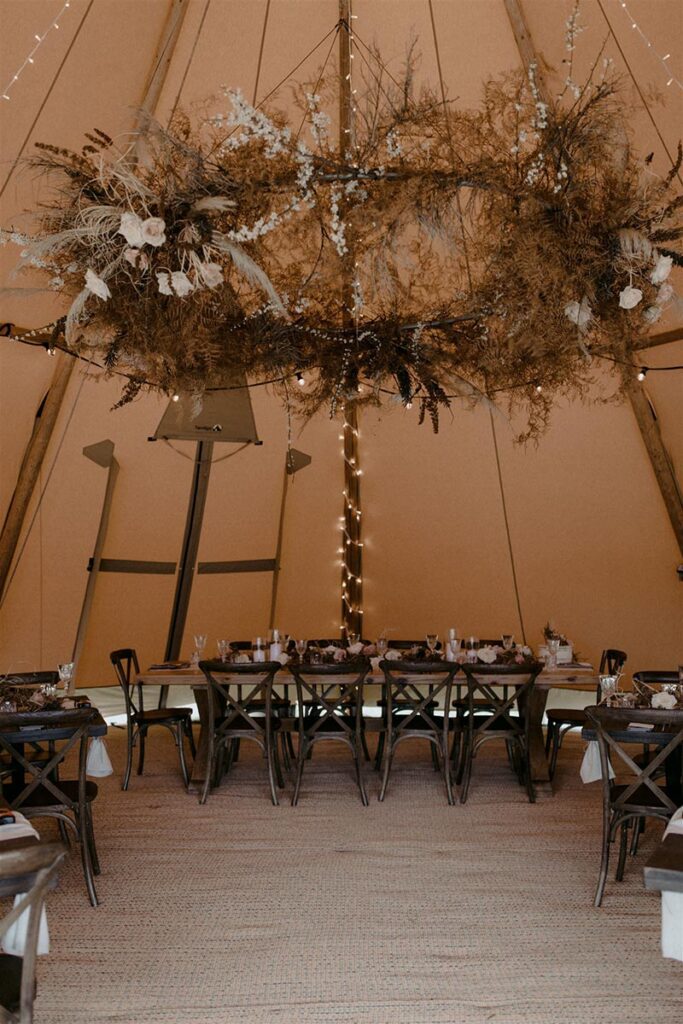 Teepee wedding reception with tables and chairs and hanging floral arrangement