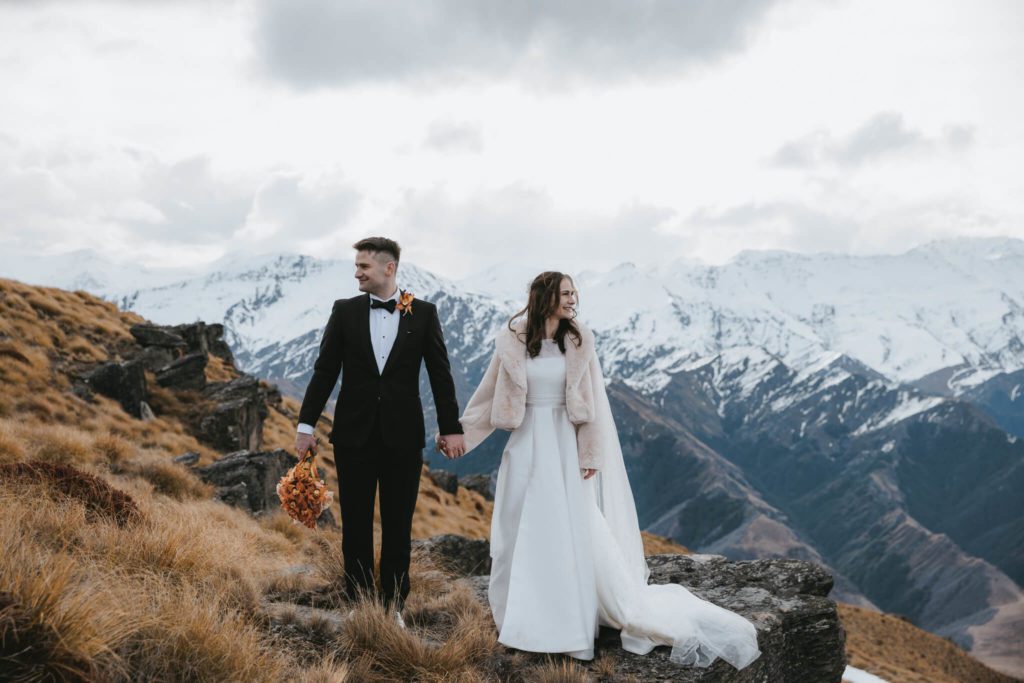 A couple stand in wedding attire in front of mountains in Queenstown