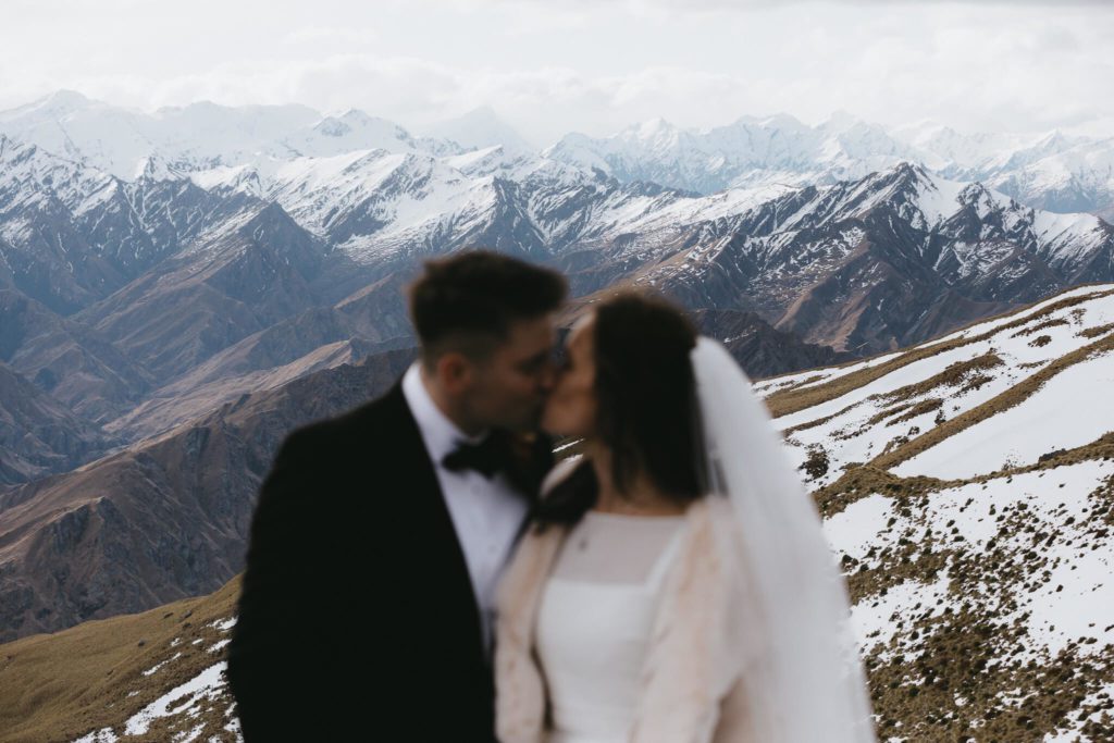 A couple kiss in wedding attire on a mountain