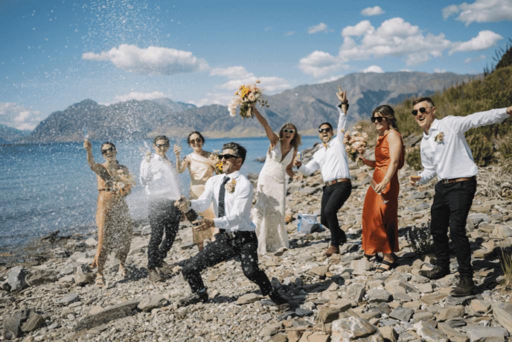 A wedding party celebrates with Champagne on a beach