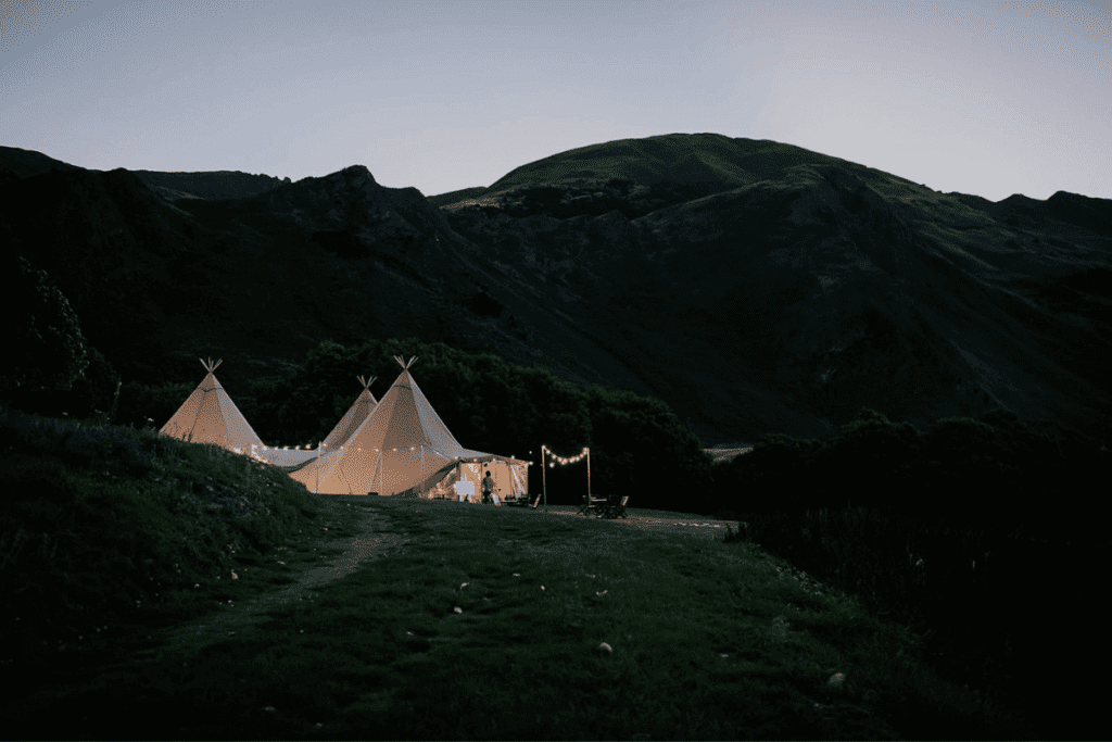 Three tipis from the side on, under mountains at nightfall